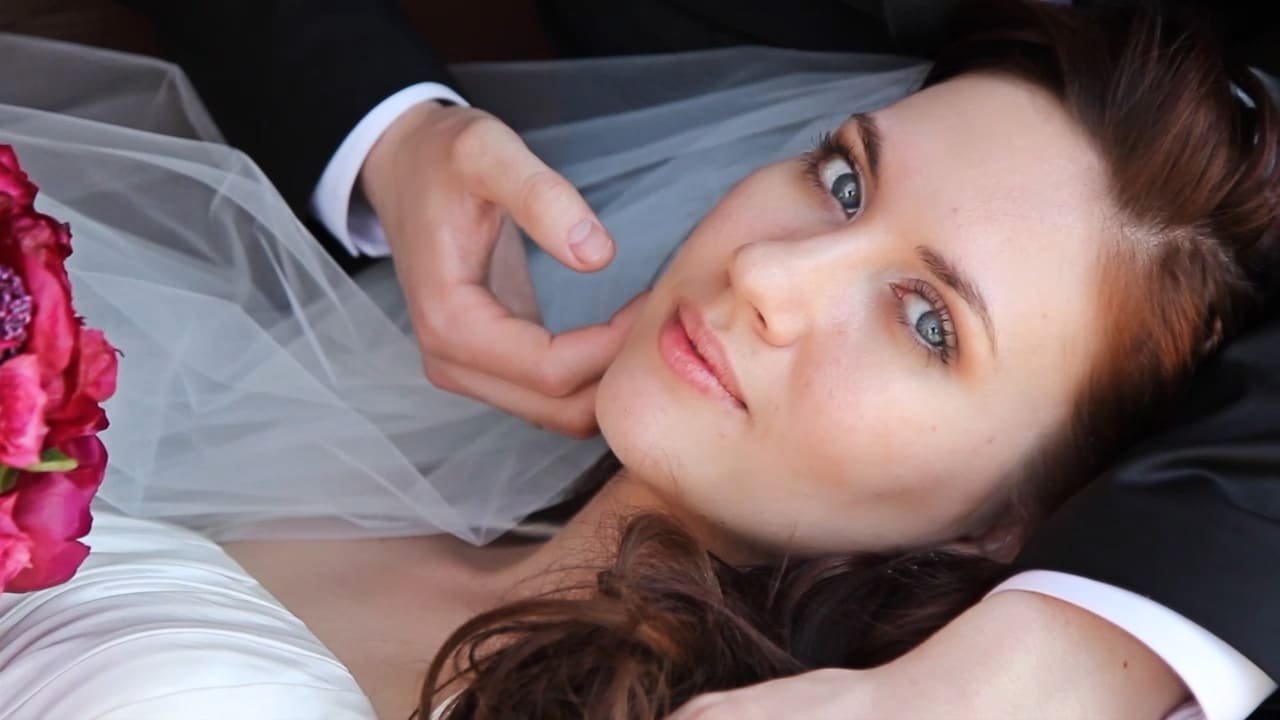 A bride and groom toast with champagne glasses, smiling at each other. The bride holds a bouquet of flowers.